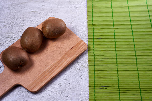 Kiwis on wooden chopping board. Stone background, bowl with several kiwis, empty space, front view, green wooden mat