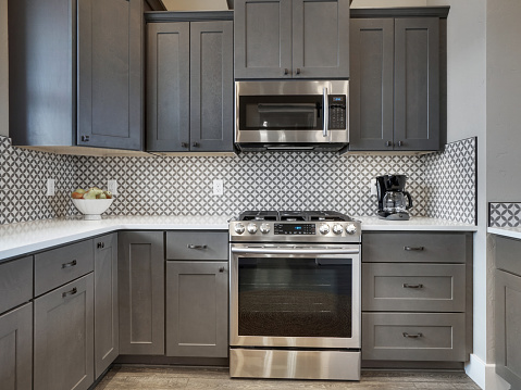 bright kitchen with modern dark wood floor and dark grey cabinets. Light white countertops with barstools, sliding barn door, modern back splash, and grey and white pattern on front side of kitchen island with new appliances