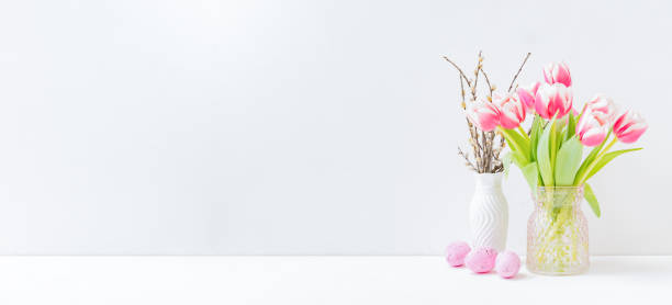 istock Home interior with easter decor. Pink tulips in a vase, easter eggs on a light background 1303903022