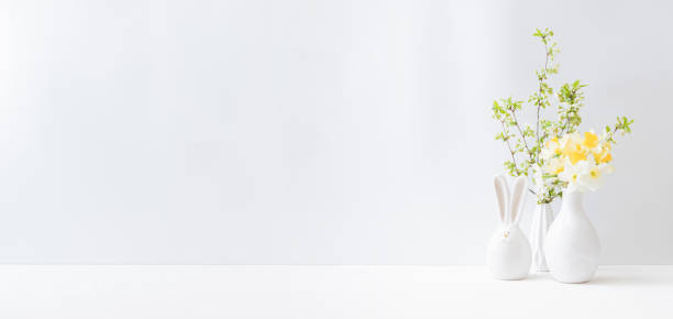istock Home interior with easter decor. Daffodils in a vase, spring flowers on a light background 1303903038