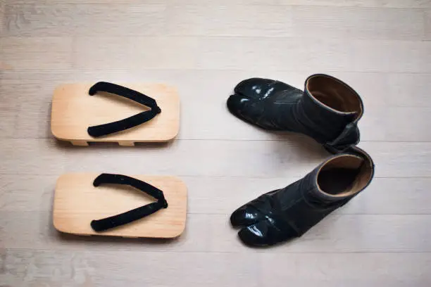 Traditional geta clogs and modern goat toe or goat hoof shoes, on light brown wooden floor