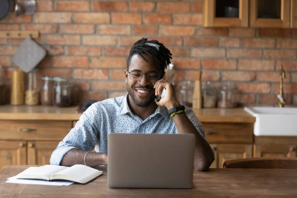 istock Smiling African American man talking on phone, using laptop 1303905746