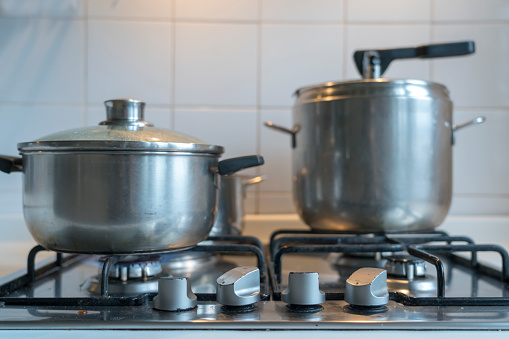 Cooking vegetable and other food on gas stove in home kitchen. Large pressure cooker and smaller pot, utensils.
