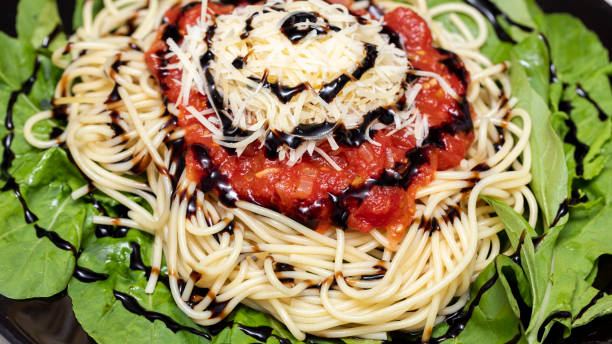 istock Spaghetti pasta with red sauce, arugula, parmesan cheese and balsamic vinegar on black plate with white marble background 1303908473