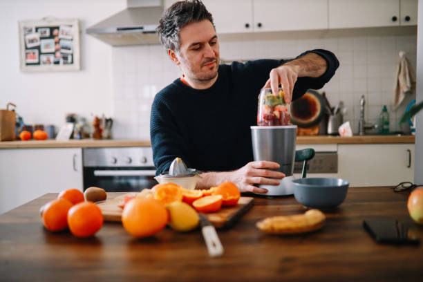 hombre preparando un batido de frutas para el desayuno en casa - blender fotografías e imágenes de stock