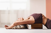 Beautiful blonde woman in sportswear, lies on a wooden block for yoga to improve posture
