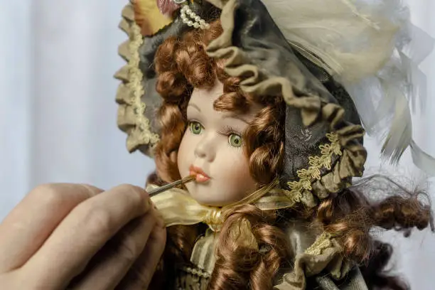 Hand carefully paints the doll's lips with a thin brush. Doll in a vintage style. Concept of combining work and hobby