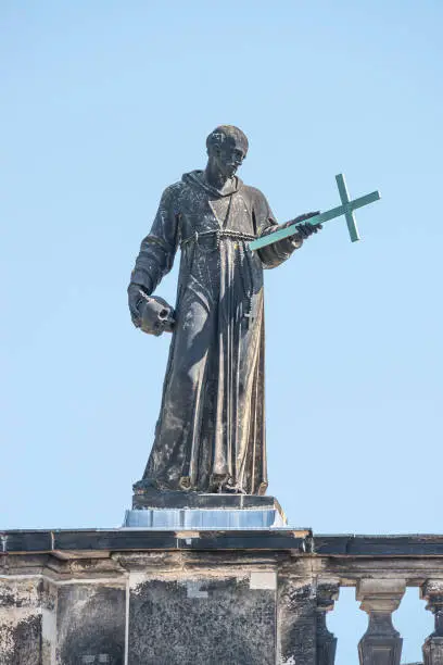 Photo of Banner with old roof church statute of high ranked priest with a cross and human skull in historical downtown of Dresden, Germany, details, closeup, with copy space for text.