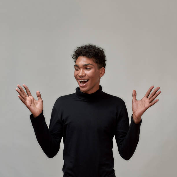 istock Happy young guy in black turtleneck smiling aside while standing with hands raised isolated over gray background 1303915558