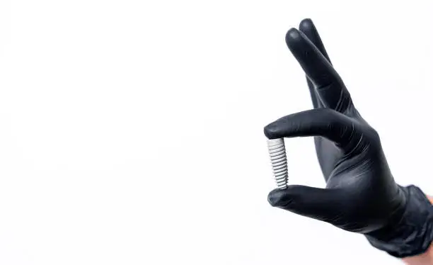 Photo of Titanium alloy bolts in hand in black latex gloves isolated on white background. Dental concept.