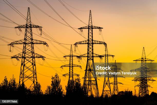 Power Pylons Reache Into The Sunset Sky Silhouettes Of Big Trees Under Energy Transmission Towers Stock Photo - Download Image Now