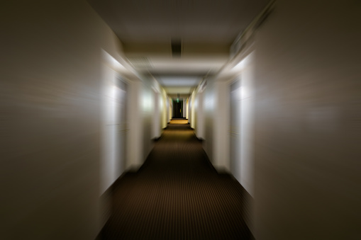 Dark Dingy Hallway - Looking down hallway with dark lighting and multiple doors with slight motion blur.