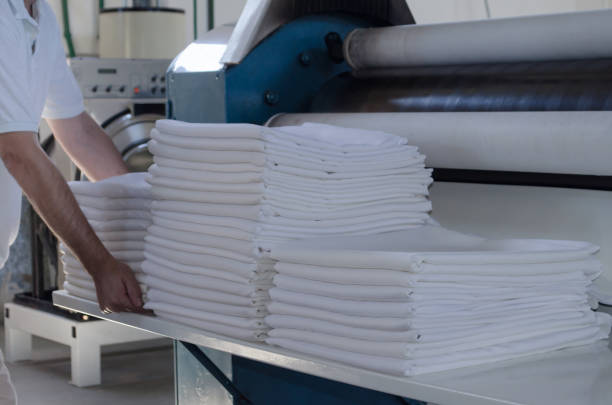 Unrecognizable man stacking freshly ironed sheets or fabrics in an industrial laundry. Cleaning and ironing service for hotels, clinics and companies.