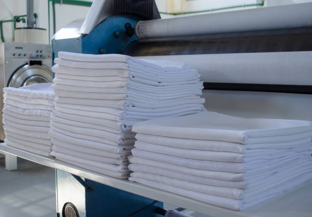istock Stack of folded clean sheets or fabrics and industrial iron in an industrial laundry. Cleaning and ironing service for hotels, clinics and companies. 1303920552