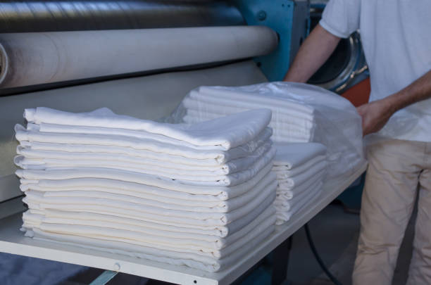 istock Unrecognizable man stacking freshly ironed sheets or fabrics in an industrial laundry. Cleaning and ironing service for hotels, clinics and companies. 1303920563