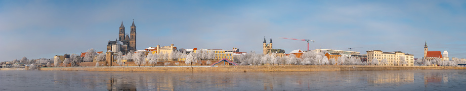 Panoramic view over Magdeburg historical downtown in Winter with icy trees and snow during sunrise in the morning with warm illumination, foggy river and blue sky, Germany