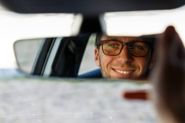 車に座りながら眼鏡をかけた陽気な楽しい男が鏡を調整し、反射を見ている。ソフトフォーカス。 - バックミラー ストックフォトと画像