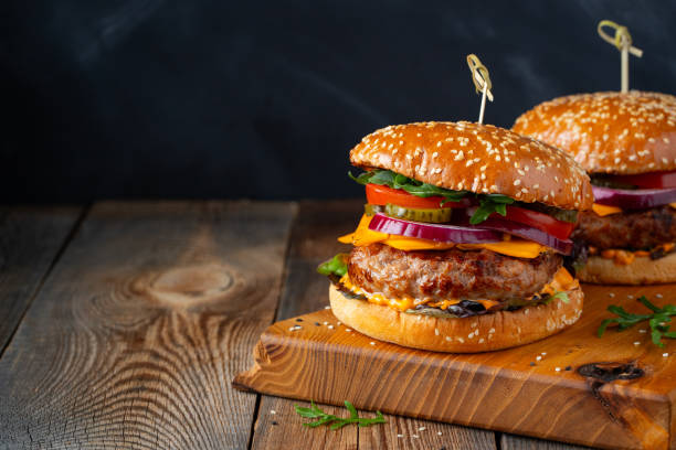 Two delicious homemade burgers of beef, cheese and vegetables on an old wooden table. Fat unhealthy food close-up. With copy space Two delicious homemade burgers of beef, cheese and vegetables on an old wooden table. Fat unhealthy food close-up. With copy space. quarter pounder stock pictures, royalty-free photos & images