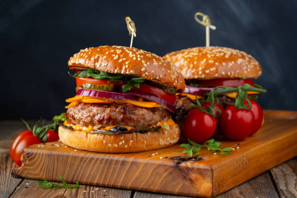 Two delicious homemade burgers of beef, cheese and vegetables on an old wooden table. Fat unhealthy food close-up Two delicious homemade burgers of beef, cheese and vegetables on an old wooden table. Fat unhealthy food close-up. quarter pounder stock pictures, royalty-free photos & images