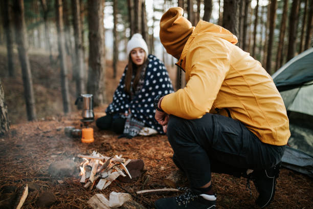 istock Boyfriend is preparing woods for fire while girlfriend making coffee in front of camping tent 1303927681