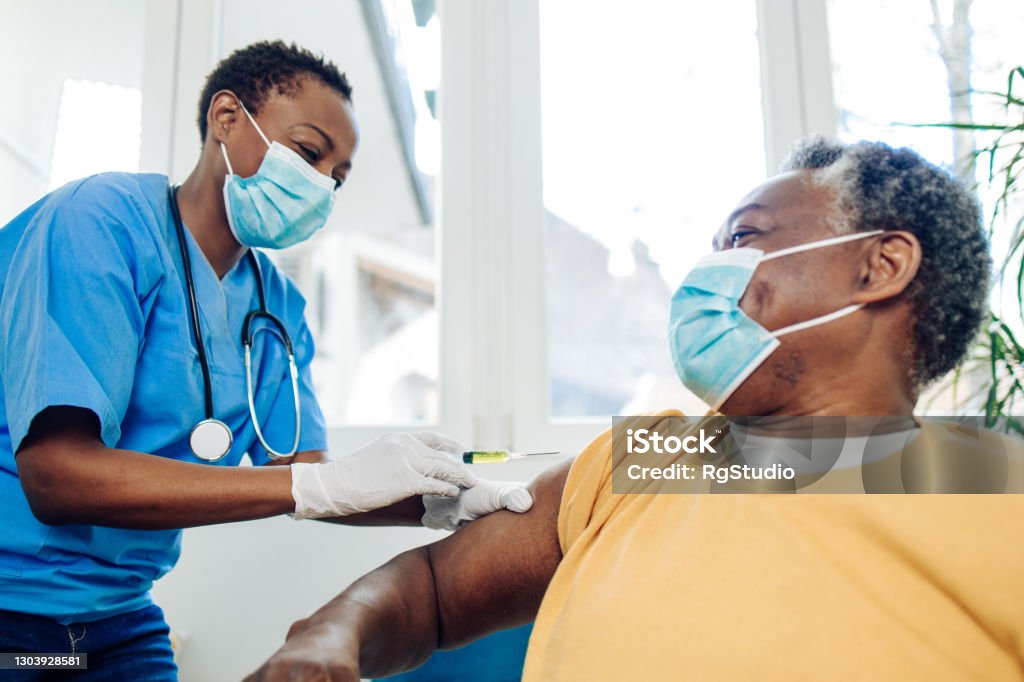African American nurse injecting a vaccine to a senior man African American senior man receiving a Covid-19 vaccine. Vaccination Stock Photo
