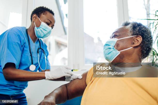 African American Nurse Injecting A Vaccine To A Senior Man Stock Photo - Download Image Now