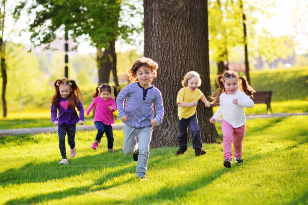 many young children smiling running along the grass in the park stock photo