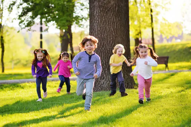 Photo of many young children smiling running along the grass in the park