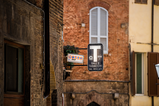 Siena, Italy - August 27, 2018: Alley street in historic medieval old town village in Tuscany with sign for lotto lottery and sali e tabacchi