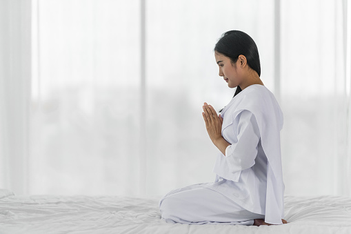 Religious Asian buddhist woman in white cloth praying and chanting with prayer hand to the statue of lord Buddha