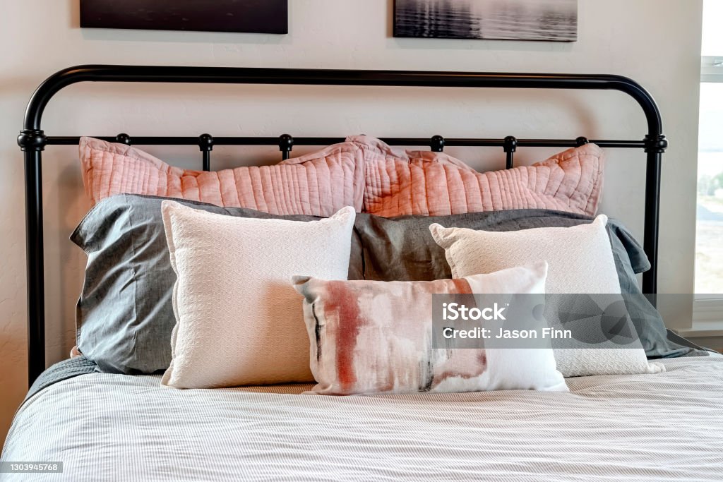 Single bed with fluffy pillows against black metal headboard inside bedroom Single bed with fluffy pillows against black metal headboard inside bedroom. Views inside a house with close up on the bed against white wall with decorations. Architecture Stock Photo