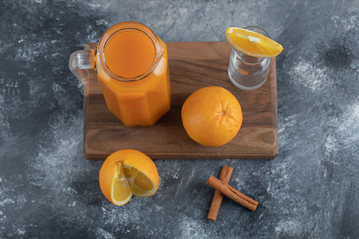 A wooden board with a glass jug of juice and orange fruits. High quality photo