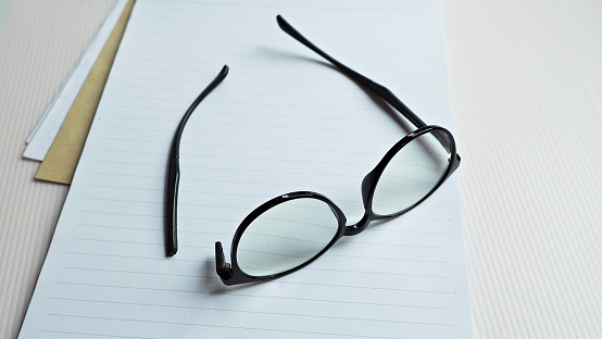 Broken eyeglasses on notepad with white background.