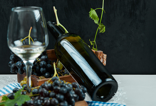 A bunch of black grapes with a glass of wine and a bottle on white table. High quality photo