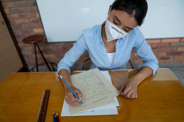 istock Teacher wearing a facemask while grading exams at the school 1303960386