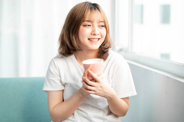The woman at home Young girl holding cup sitting by glass door in early morning hot filipina women stock pictures, royalty-free photos & images