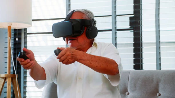 Asian senior man having fun playing video game with virtual reality glasses at home.
