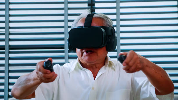 istock Asian senior man having fun playing video game with virtual reality glasses at home. 1303966334