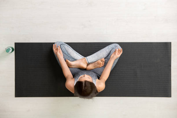 view of young brunette sportswoman in tracksuit sitting on mat in pose of lotus - yoga meditating women exercise mat imagens e fotografias de stock