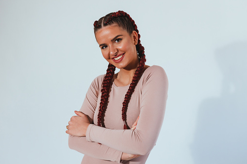 Portrait of a beautiful young smiling woman with braided hair wearing a nude color blouse against bright background