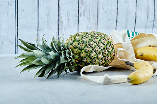 Ripe pineapple and banana in a white bag on blue background. High quality photo