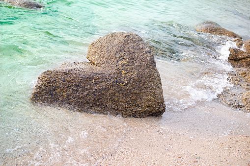 Stone heart shape nature authentic on sand beach and soft wave blue sea at coast. romantic love valentine days, broken heart or tourist travel summer in holidays.