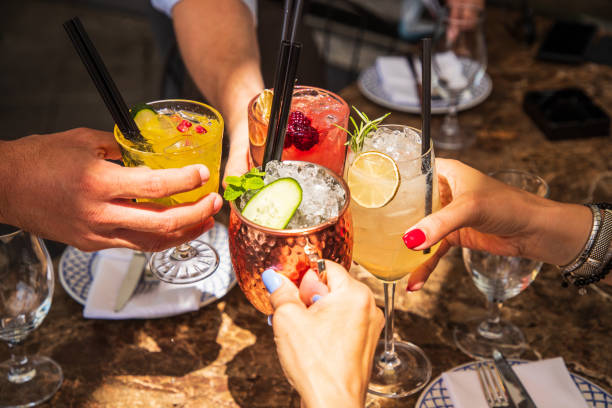 Four hands holding coctails on ice in celebratory toast at the table stock photo