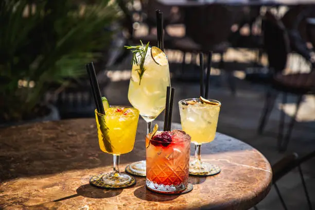 Four cocktails on ice in drinking glasses served on coasters on marble table in the bar garden