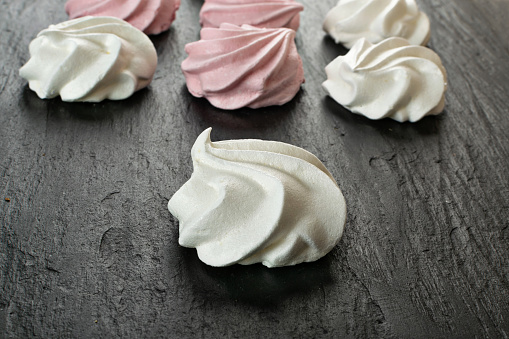 White and pink meringue cookies closeup. Traditional whisk merengues, baked whisking cream or beze on blurred background