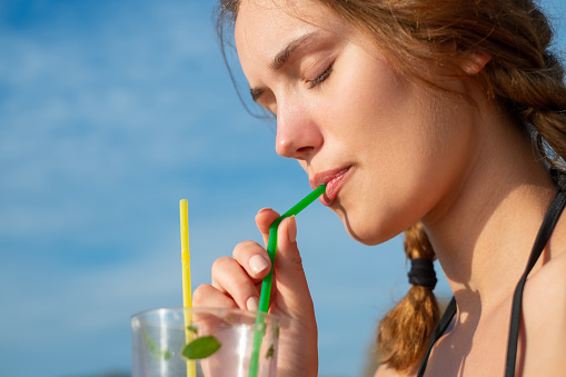Beautiful young woman enjoying a tropical mojito cocktail, sipping it through a straw on summer vacation