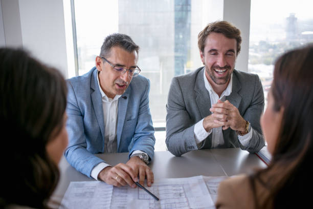 istock Two businessmen in a meeting analyzing project on spreadsheet with female partners 1303981636