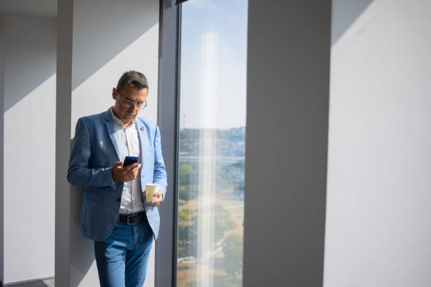 istock Businessman standing on coffee break by the big office window and texting 1303981717