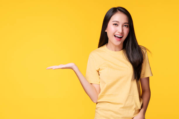 istock Cheerful young woman holding her hand with product or empty copy space while standing over isolated on yellow background 1303984235