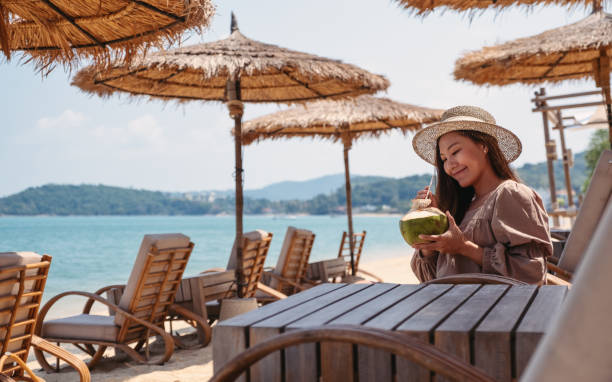 a beautiful young asian woman holding and drinking coconut juice on the beach
